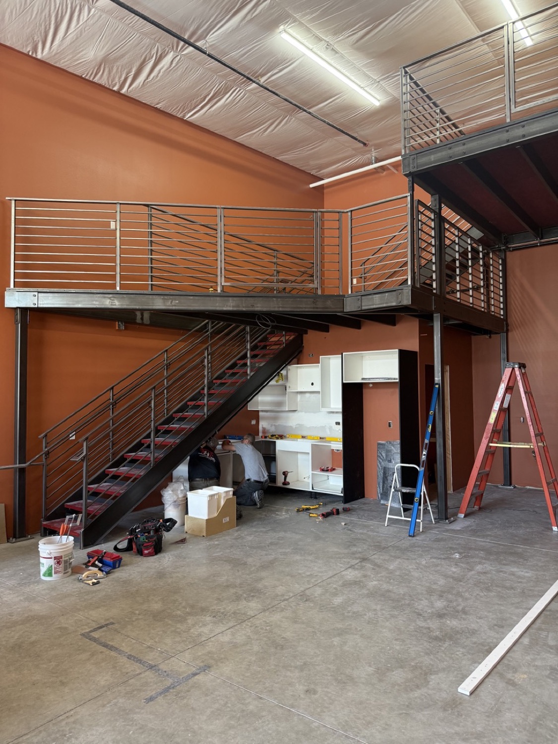 Custom mezzanine loft with wraparound railings, stairs, and space below for a workshop